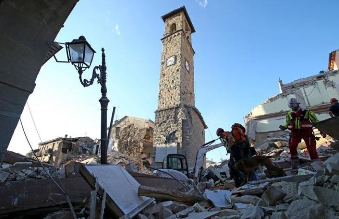 Rescuers walk past the bell tower with the clock showing the time of the earthquake in Amatrice, central Italy, August 24, 2016.