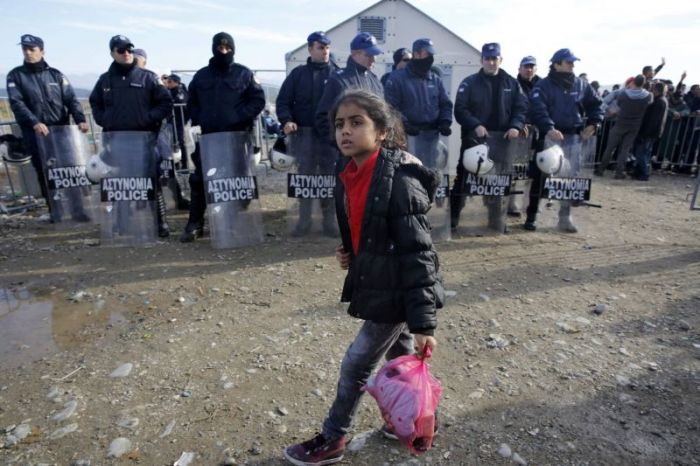 A Syrian refugee girl walks by Greek police before crossing the border from Greece to Macedonia near the Greek village of Idomeni in this undated photo.