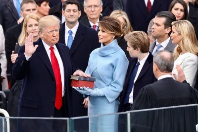 President Donald Trump being sworn in on January 20, 2017 at the U.S. Capitol building in Washington, D.C. Melania Trump wears a sky-blue cashmere Ralph Lauren ensemble. He holds his left hand on two versions of the Bible, one childhood Bible given to him by his mother, along with Abraham Lincoln's Bible.
