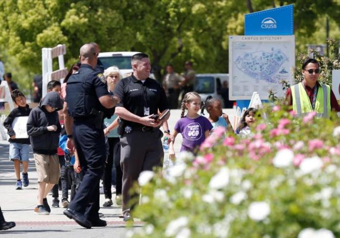 Police officers escort students from a campus of California State University - San Bernardino, where they were evacuated after a shooting at North Park Elementary School, to be reunited with their parents in San Bernardino, California, U.S. April 10, 2017.