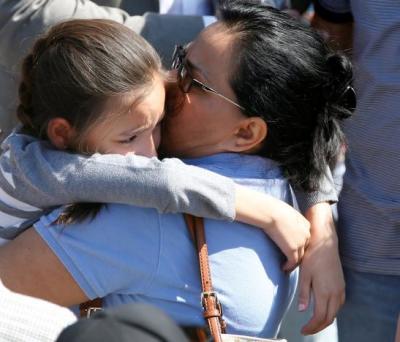 A student who was evacuated after a shooting at North Park Elementary School is embraced after groups of them were reunited with parents waiting at a high school in San Bernardino, California, U.S. April 10, 2017.