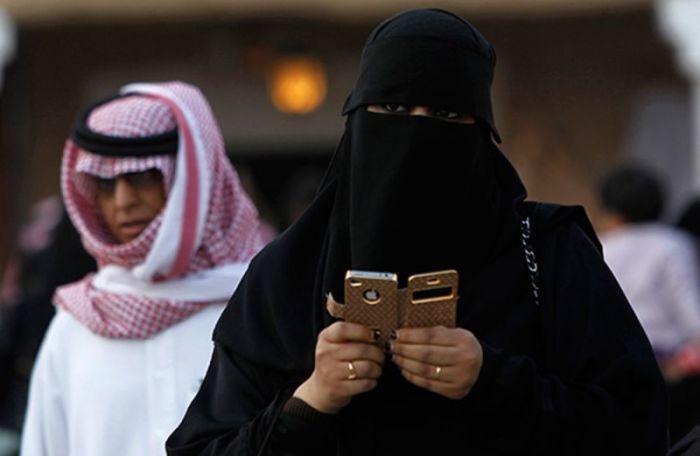 A member of the Saudi religious police warily eyes a woman holding a cell phone inside a mall in Saudi Arabia.