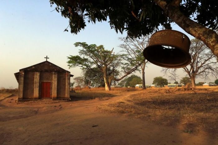A church bell hangs from a tree branch outside a Catholic church and a school in Odek village, Uganda.