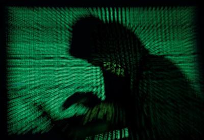 A hooded man holds a laptop computer as cyber code is projected on him in this illustration picture taken on May 13, 2017.