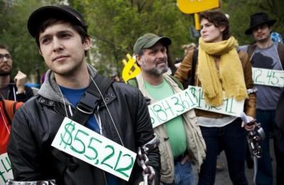 Occupy Wall Street demonstrators participating in a street-theater production wear signs around their neck representing their student debt during a protest against the rising national student debt in Union Square, in New York, April 25, 2012.