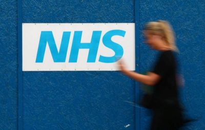 A woman passes an NHS sign at The Royal London Hospital in London, Britain.