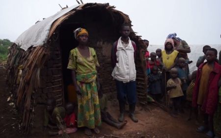 A displaced family in the Democratic Republic of Congo pose behind their humble shack.