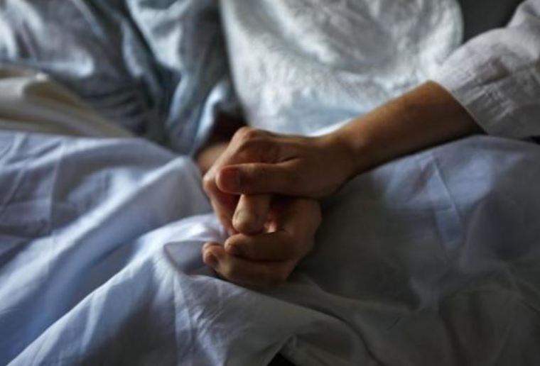 A photo of a woman holding the hand of her mother who is dying from cancer during her final hours at a palliative care hospital in Winnipeg.