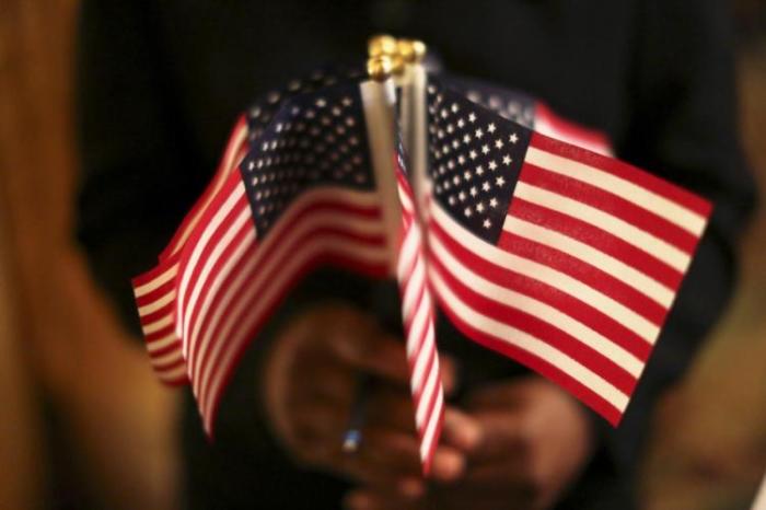 A woman holds a cluster of U.S. flags during a U.S. Citizenship and Immigration Services naturalization ceremony.