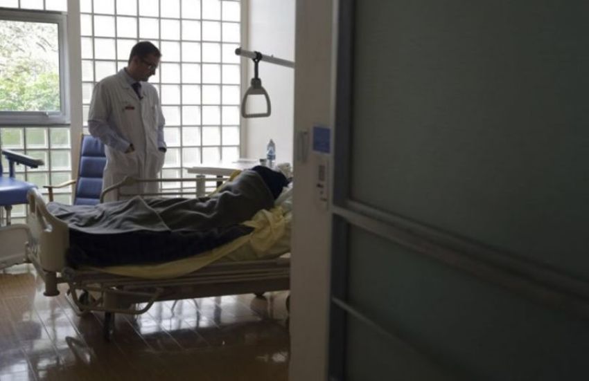 A doctor looks down at a patient in a hospital bed.