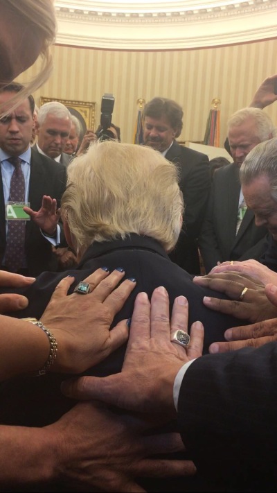 A group of evangelical leaders lay hands on President Donald Trump and pray over him at a White House Oval Office meeting on Monday, July 10, 2017.