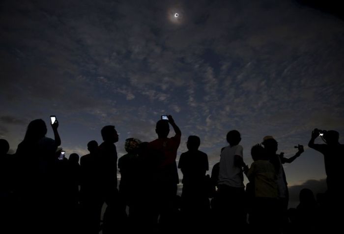 People watch and take pictures of the solar eclipse on a beach in Ternate, Indonesia.