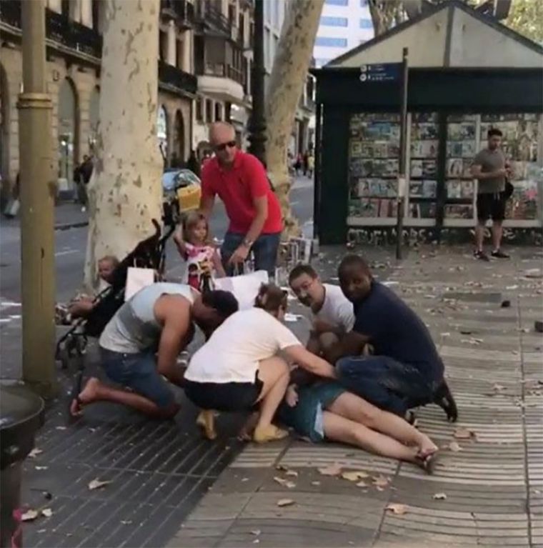 People help an injured woman lying on the ground after a van crashed into pedestrians near the Las Ramblas avenue in central Barcelona, Spain, August 17, 2017.