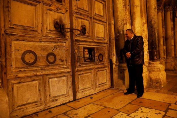 Adeeb Joudeh (R), a Muslim who says his family were entrusted as the custodians of the ancient key to the Church of the Holy Sepulchre, looks at a priest through the church doors in Jerusalem's Old City on November 3, 2017.