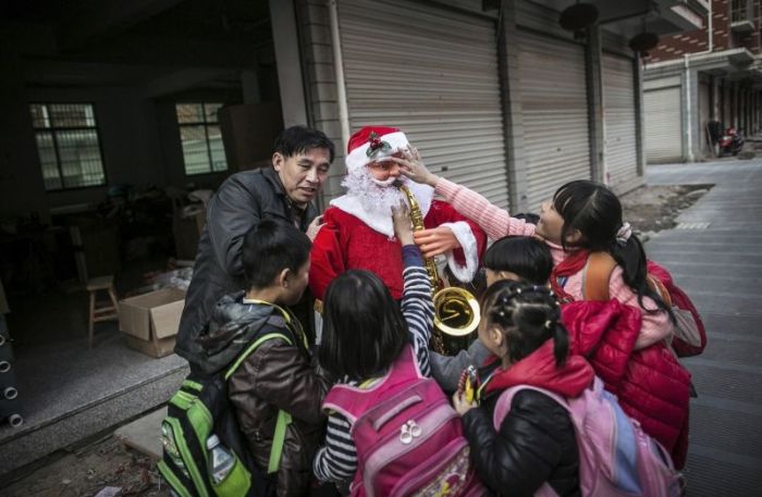 A worker holding a newly made Santa Claus model is surrounded by students in Yiwu, Zhejiang province December 4, 2014.