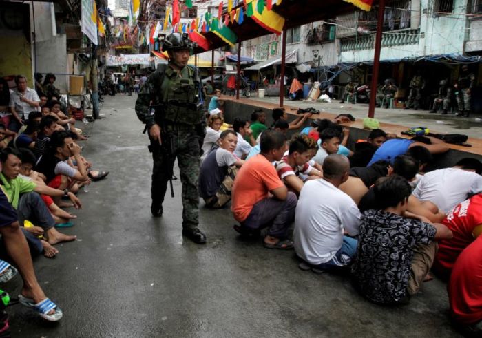 People sit on a street after they were rounded up to be brought to a police station for verification if they are involved with drugs in Manila, Philippines.
