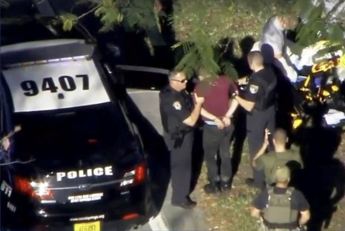 A man placed in handcuffs is led by police near Marjory Stoneman Douglas High School following a shooting incident in Parkland, Florida, February 14, 2018, in a still image from video.