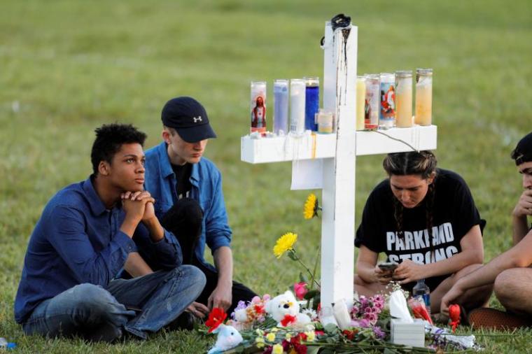 Mourners sit around one of 17 crosses at a memorial for the victims of the shooting at Marjory Stoneman Douglas High School in Parkland, Florida, February 16, 2018.
