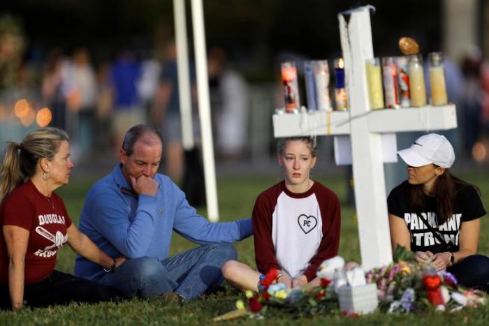 A family sits around one of 17 crosses at a memorial for the victims of the shooting at Marjory Stoneman Douglas High School in Parkland, Florida, February 16, 2018.
