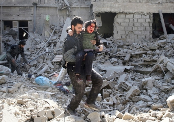 A man carries an injured boy as he walks on rubble of damaged buildings in the rebel-held besieged town of Hamouriyeh in Eastern Ghouta in February 2018.