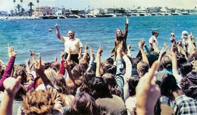 Chuck Smith (left) raising his hand and Lonnie Frisbee (right) along the edge of Newport Harbor