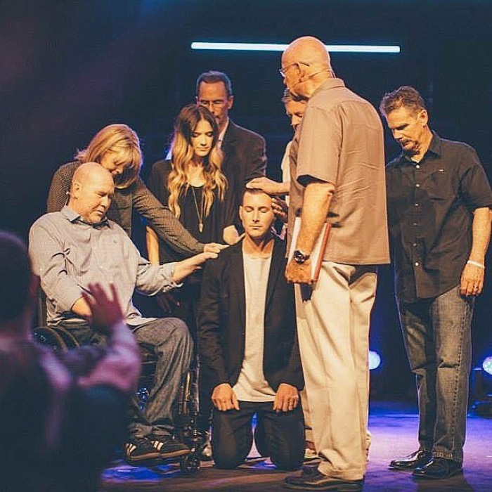 Andrew Stoecklein, 30 (kneeling), the late pastor of Inland Hills Church in Chino, Calif., is blessed by his father Dave Stoecklein (wheelchair) and other members of his church and immediate family in May 2015 as he becomes lead pastor. His father who was suffering from leukemia at the time, died in October that year.