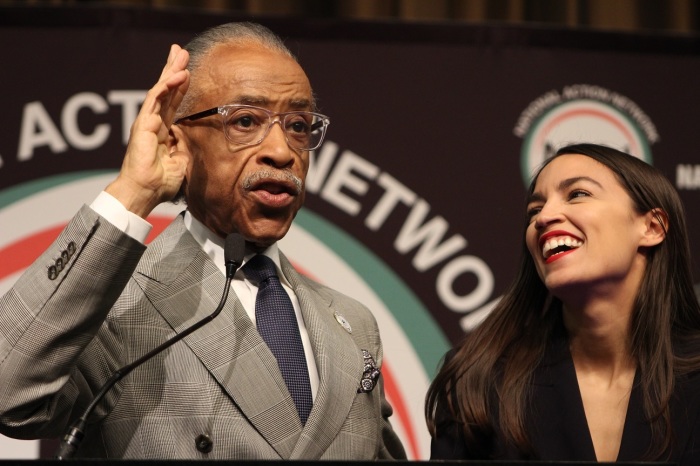 Rep. Alexandria Ocasio-Cortez, D-N.Y., (R) laughs at the National Action Network convention in New York on Friday April 5, 2019 as founder Rev. Al Sharpton shares a joke with the crowd.