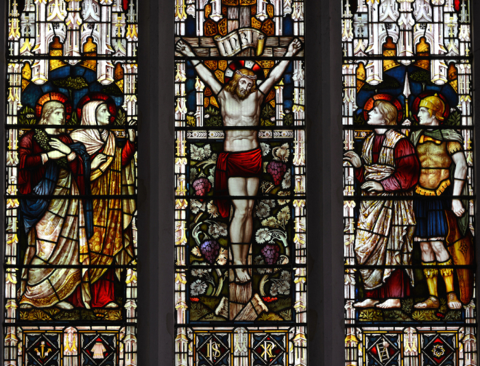 A Victorian 19th century stained glass window in an ancient English church, depicting the crucifixion of Jesus Christ.