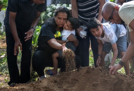 A woman holds a crying child as she throws earth onto a coffin during a funeral for a person killed in the Easter Sunday attack on St Sebastian's Church, on April 23, 2019 in Negombo, Sri Lanka.