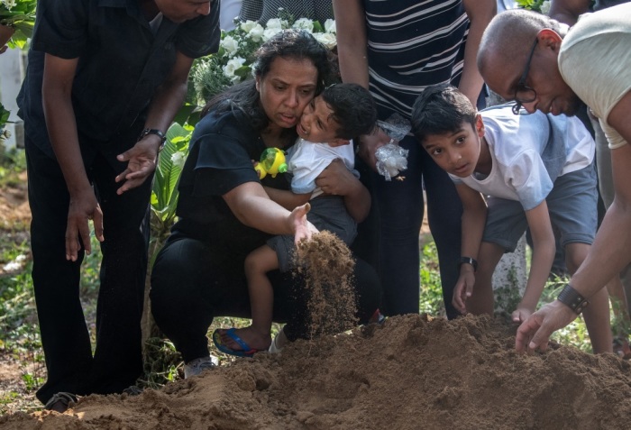 A woman holds a crying child as she throws earth onto a coffin during a funeral for a person killed in the Easter Sunday attack on St Sebastian's Church, on April 23, 2019 in Negombo, Sri Lanka. 