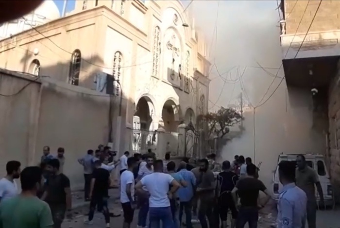 By standards look at the aftermath of a car bombing that took place outside the Syriac Orthodox Church of St. Mary in Qamishli, Syria on July 11, 2019. 