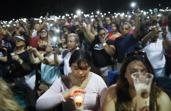 People hold up their phones in lieu of candles at an interfaith vigil for victims of a mass shooting, which left at least 20 people dead, on August 4, 2019 in El Paso, Texas. A 21-year-old male suspect was taken into custody in the city which sits along the U.S.-Mexico border. At least 26 people were wounded. 