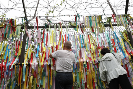 Visitors look through a wire fence covered with prayer ribbons wishing for reunification of the two Koreas. Photo taken at Imjingak, near the demilitarized zone in Paju, South Korea, on June 20, 2019.