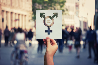 Hand holding a paper sheet with transgender symbol and equal sign inside.