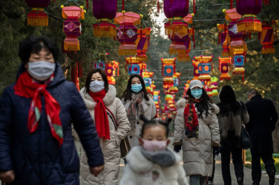 Chinese women and a child all wear protective masks as they walk under decorations in a park after celebrations for the Chinese New Year and Spring Festival were cancelled by authorities on January 25, 2020, in Beijing, China. 