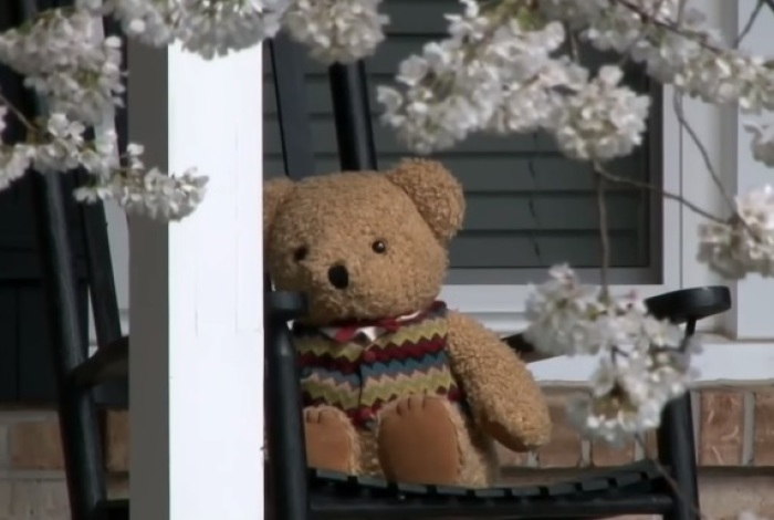 A teddy bear sits on a porch as part of the 'Teddy Bear Hunt' initiative. 