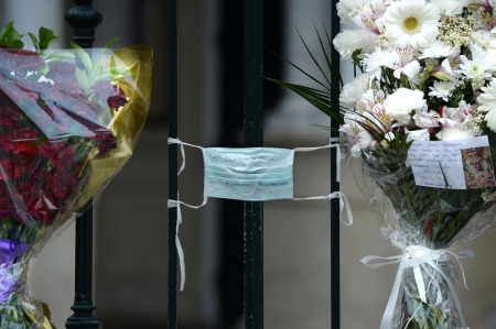 A face mask with the text 'You, the one who can do anything, help us, please' is tied to the fence of La Macarena church on April 9, 2020, in Seville, Spain, adorned with flowers left by the faithful after Easter processions were cancelled during a national lockdown to prevent the spread of the COVID-16 disease.
