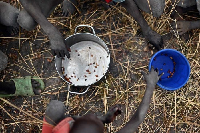 Children collect grain spilt on the field from gunny bags that ruptured upon ground impact following a food drop from a plane at a village in Ayod county, South Sudan, where World Food Program have just carried out a food drop of grain and supplementary aid on February 6, 2020.