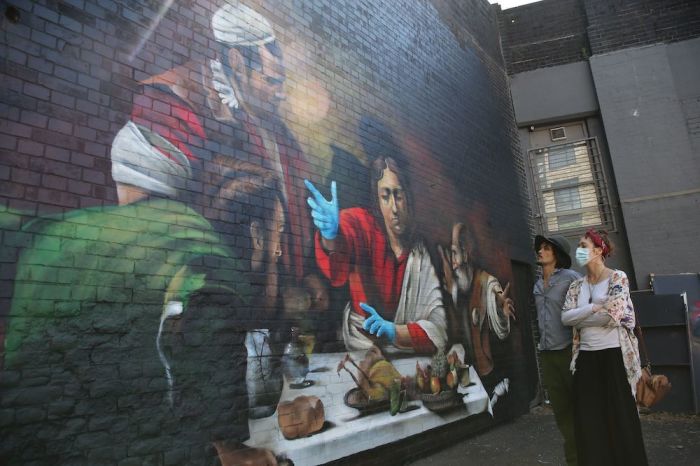 A couple look at a mural by artist Lionel Stanhope depicting the painting 'The Supper at Emmaus' by Italian painter Caravaggio with the addition of blue nitrile gloves in south London on May 6, 2020 as life continues under a nationwide lockdown imposed to slow the spread of the novel coronavirus. 