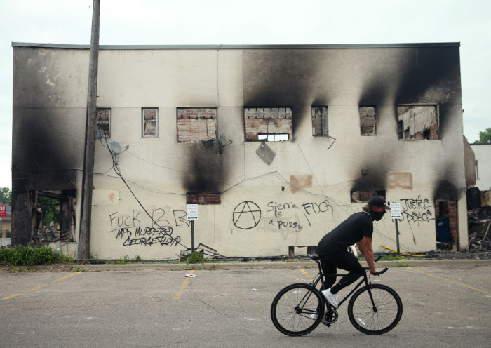A man rides a bicycle past a burned-out building after a night of protests and violence on May 29, 2020, in Minneapolis, Minnesota. The National Guard has been activated as protests continue after the death of George Floyd, which has caused widespread destruction and fires across Minneapolis and St. Paul. 