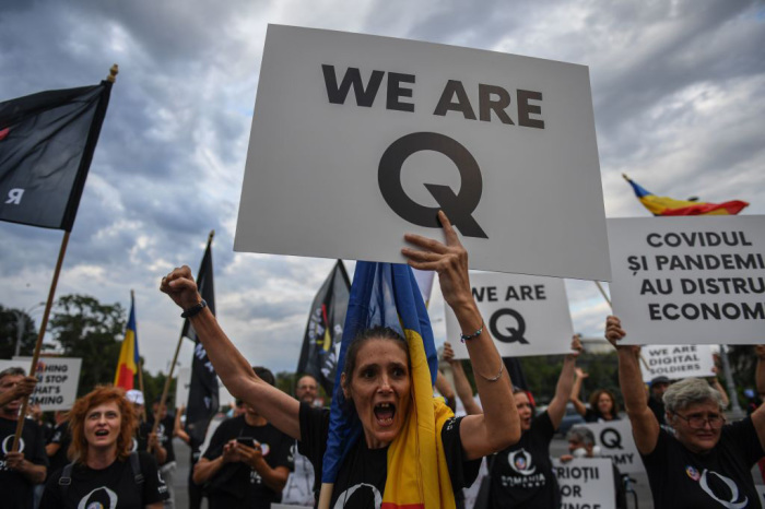 A woman shouts as she holds a placard reading 'Q Army' (a reference to the Q-anon movement), during a protest against government lockdowns and the shutting down of businesses in response to the coronavirus pandemic in front of the Romanian Government headquarters August 10, 2020.