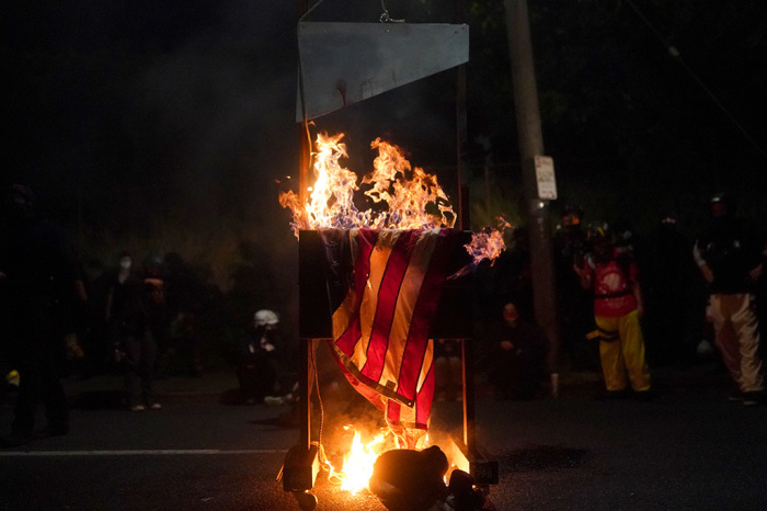 An American flag burns on a guillotine in front of the Multnomah County Sheriffs Office on August 22, 2020, in Portland, Oregon. Hundreds of rioters clashed with police Saturday night following a rally in east Portland. 