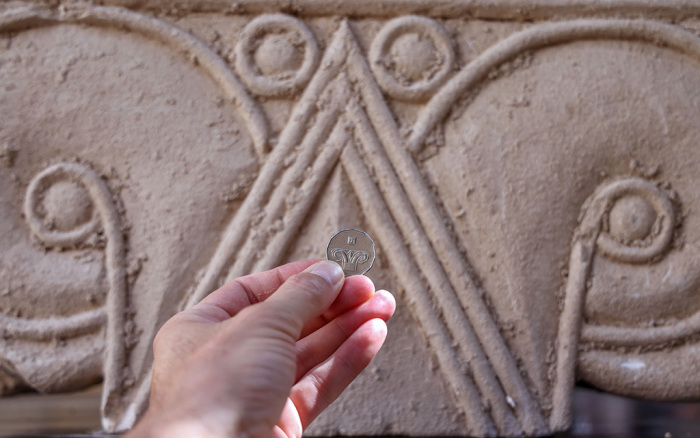 An Israeli five shekels coin is held in front of a column capital displaying the same decorative carvings, as part of a collection of several dozen adorned architectural stone artifacts estimated to date from around 701 BC, are unveiled during a press presentation in Jerusalem on September 3, 2020. The stone artifacts, made of soft limestone with decorative carvings in the architectural style known as 'Proto-Aeolian,' are thought to be part of an expensive structure built on a hillside overlooking Jerusalem's old city in the period between the days of King Hezekiah and King Josiah. The importance of the decorative carvings from this period led the Bank of Israel to choose it as the image that adorns the Israeli five shekel coin. 