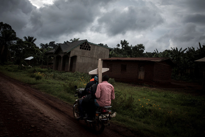 Three Congolese ride a motorbike and carry a cross for a grave along the road linking Mangina to Beni on August 23, 2018, in Mangina, in the North Kivu province. 