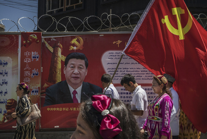 Ethnic Uyghur members of the Communist Party of China carry a flag past a billboard of Chinese President Xi Jinping as they take part in an organized tour on June 30, 2017, in the old town of Kashgar, in the far western Xinjiang province, China. Kashgar has long been considered the cultural heart of Xinjiang for the province's nearly 10 million Muslim Uyghurs. 
