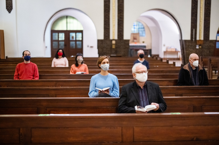 People wearing protective face masks sitting with social distance and attending religious mass at church. 