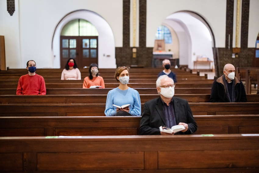 People wearing protective face masks sitting with social distance and attending religious mass at church.