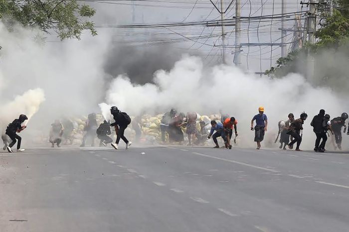 Protesters run from tear gas fired by security forces, as some demonstrators also let off fire extinguishers, next to a barricade set up during the demonstration against the military coup in Mandalay on March 15, 2021. 