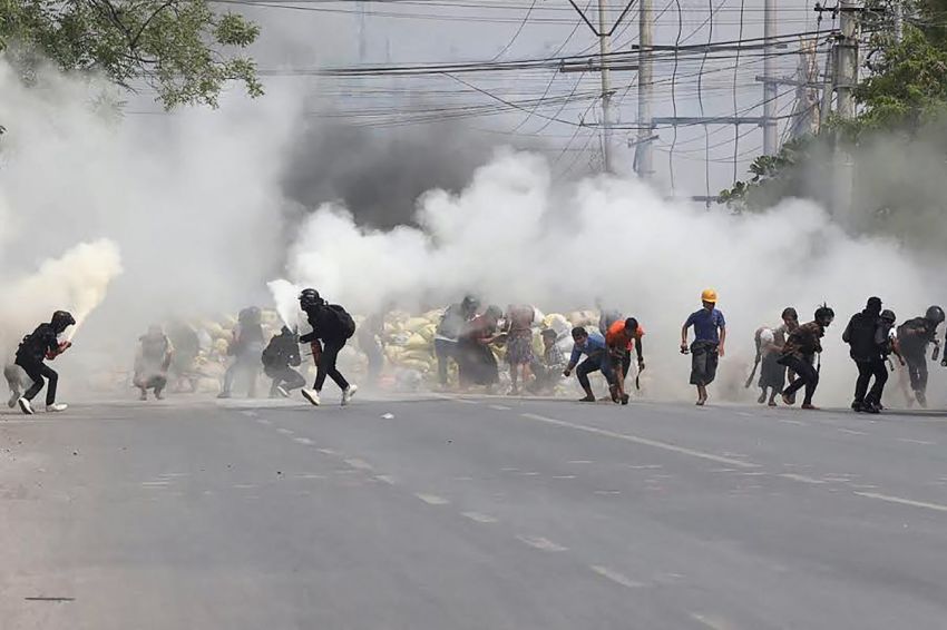 Protesters run from tear gas fired by security forces, as some demonstrators also let off fire extinguishers, next to a barricade set up during the demonstration against the military coup in Mandalay on March 15, 2021.