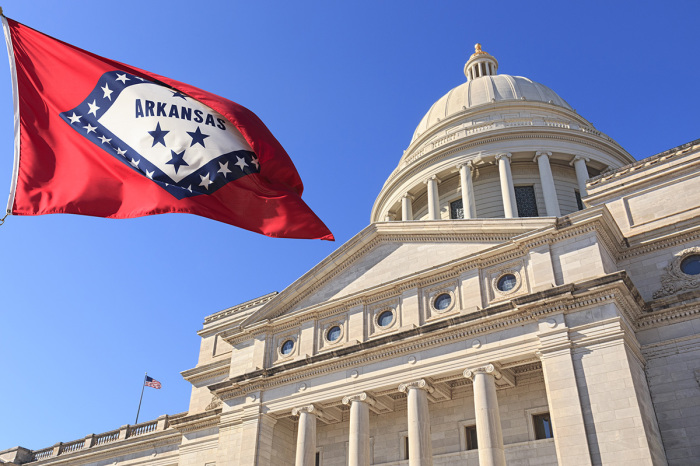 Arkansas flag flying high beside the Arkansas state Capitol, front exterior, in Little Rock, Arkansas.